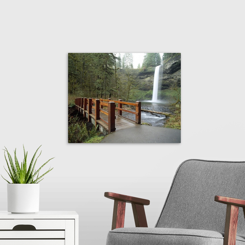 A modern room featuring Large wall docor of a wooden bridge going across a river with a thin waterfall on the right.
