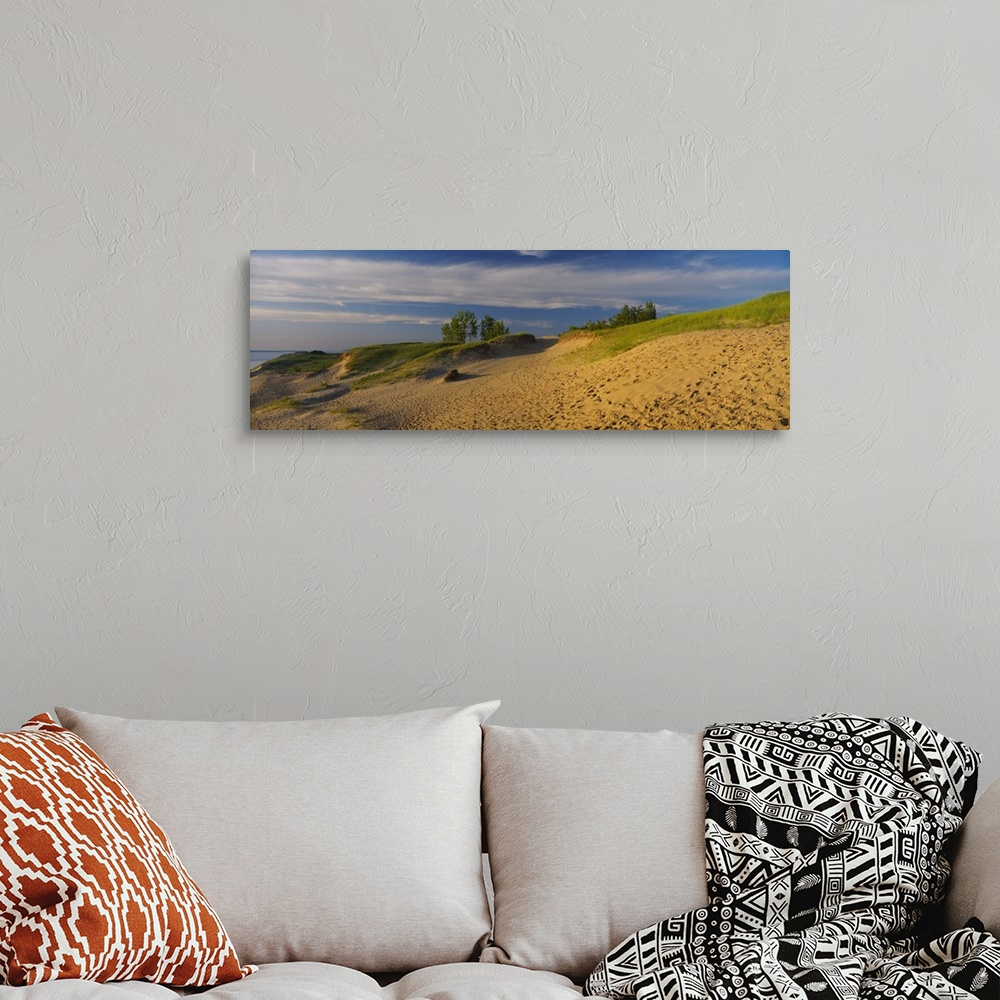 A bohemian room featuring Sloping sand dunes covered in beach grass and footprints under wispy clouds at sunset at the edge...