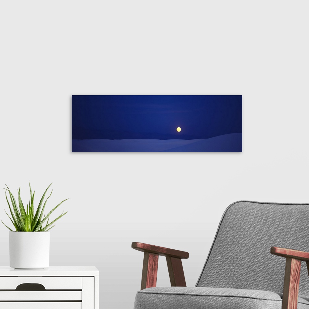 A modern room featuring Panoramic photograph taken of a full moon against a deep blue sky and sitting above white sand th...