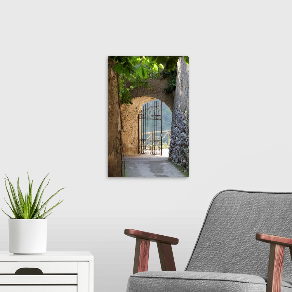A modern room featuring A vertical photograph of a walkway lined with old masonry a green vines to an open iron wrought g...
