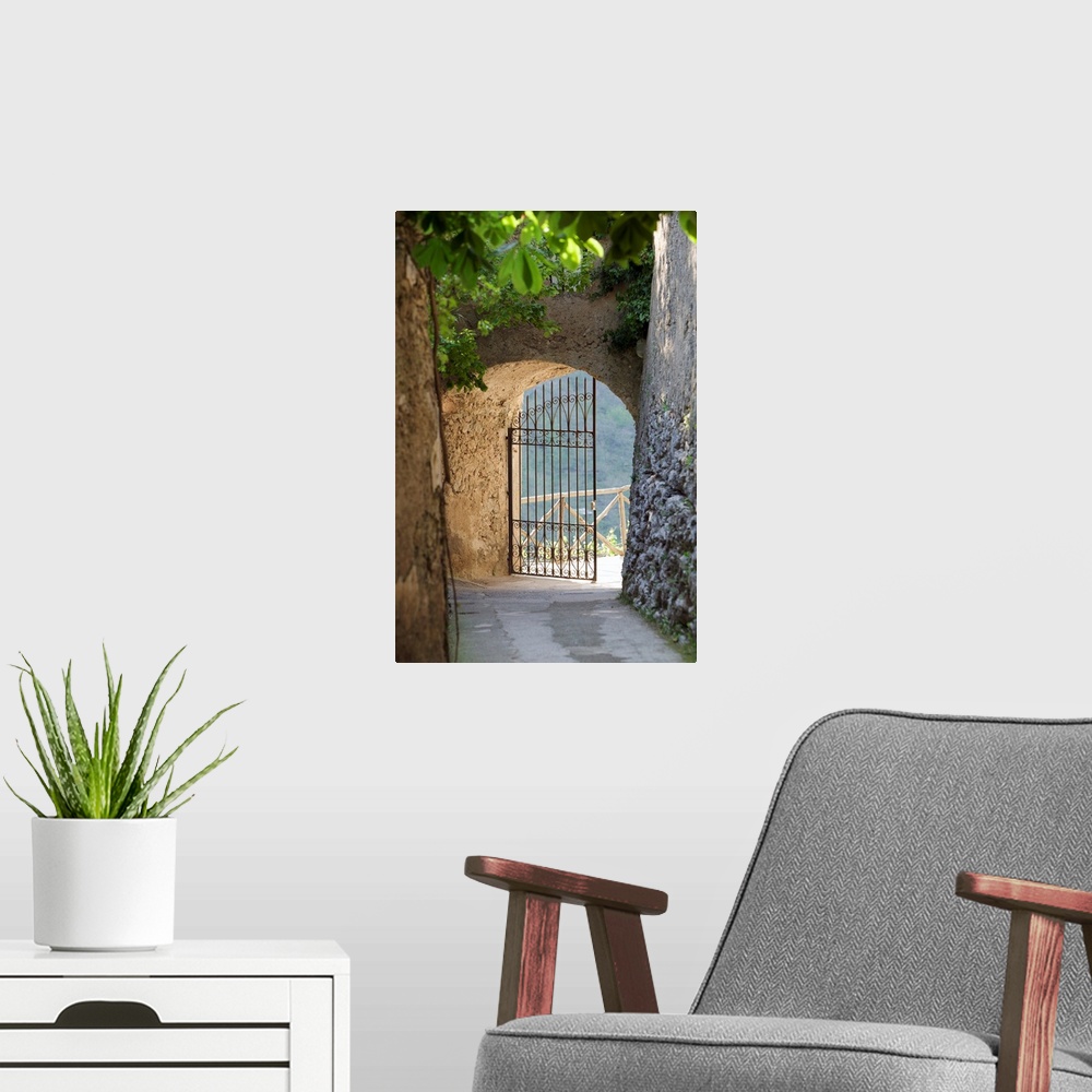 A modern room featuring A vertical photograph of a walkway lined with old masonry a green vines to an open iron wrought g...