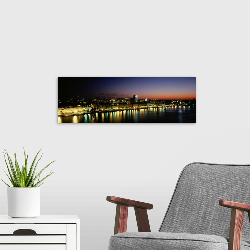 A modern room featuring Panoramic photograph of lit up skyline and waterfront at sunset under a colorful sky.
