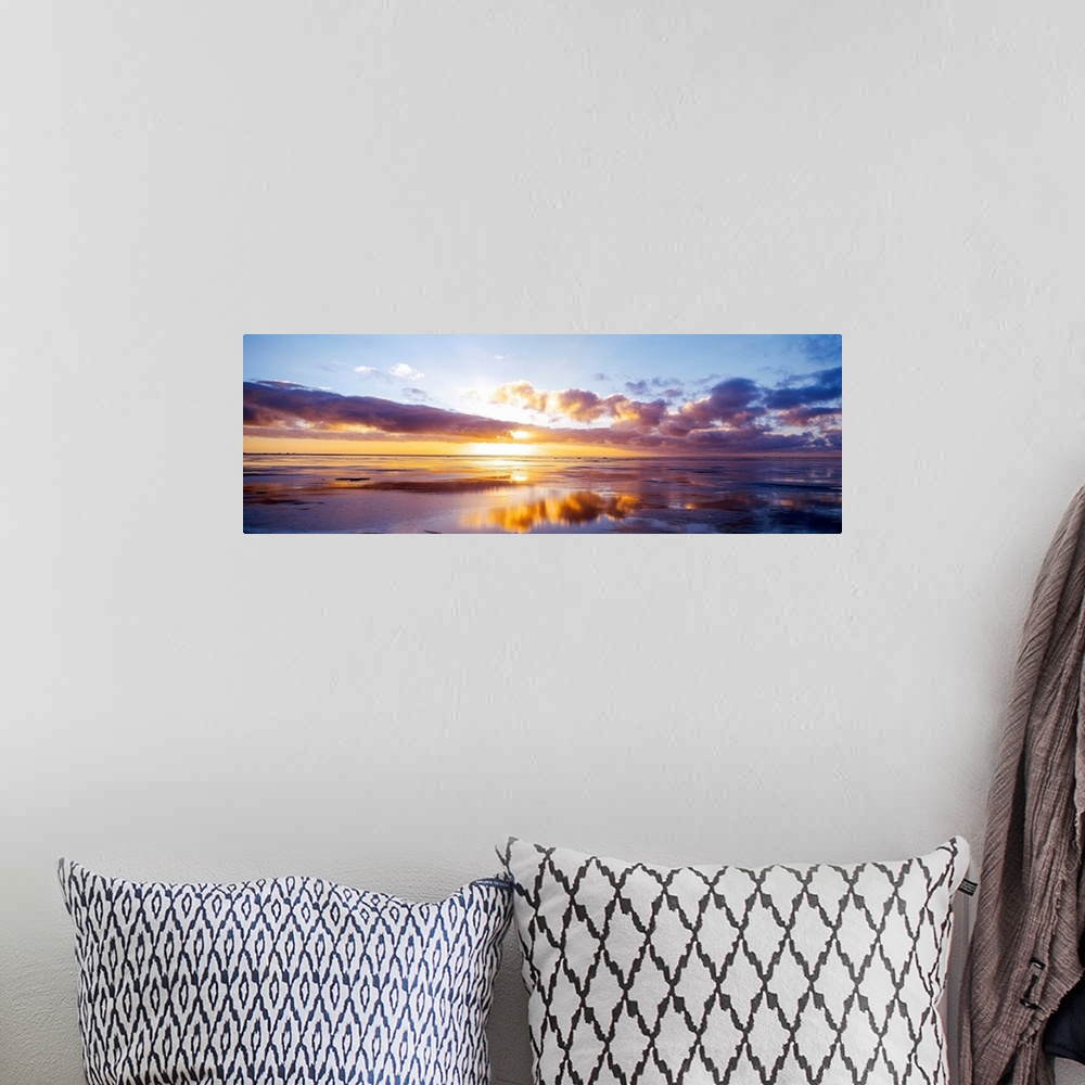 A bohemian room featuring The sun breaks over the clouds in the horizon in this large panoramic photo from a beach on the N...