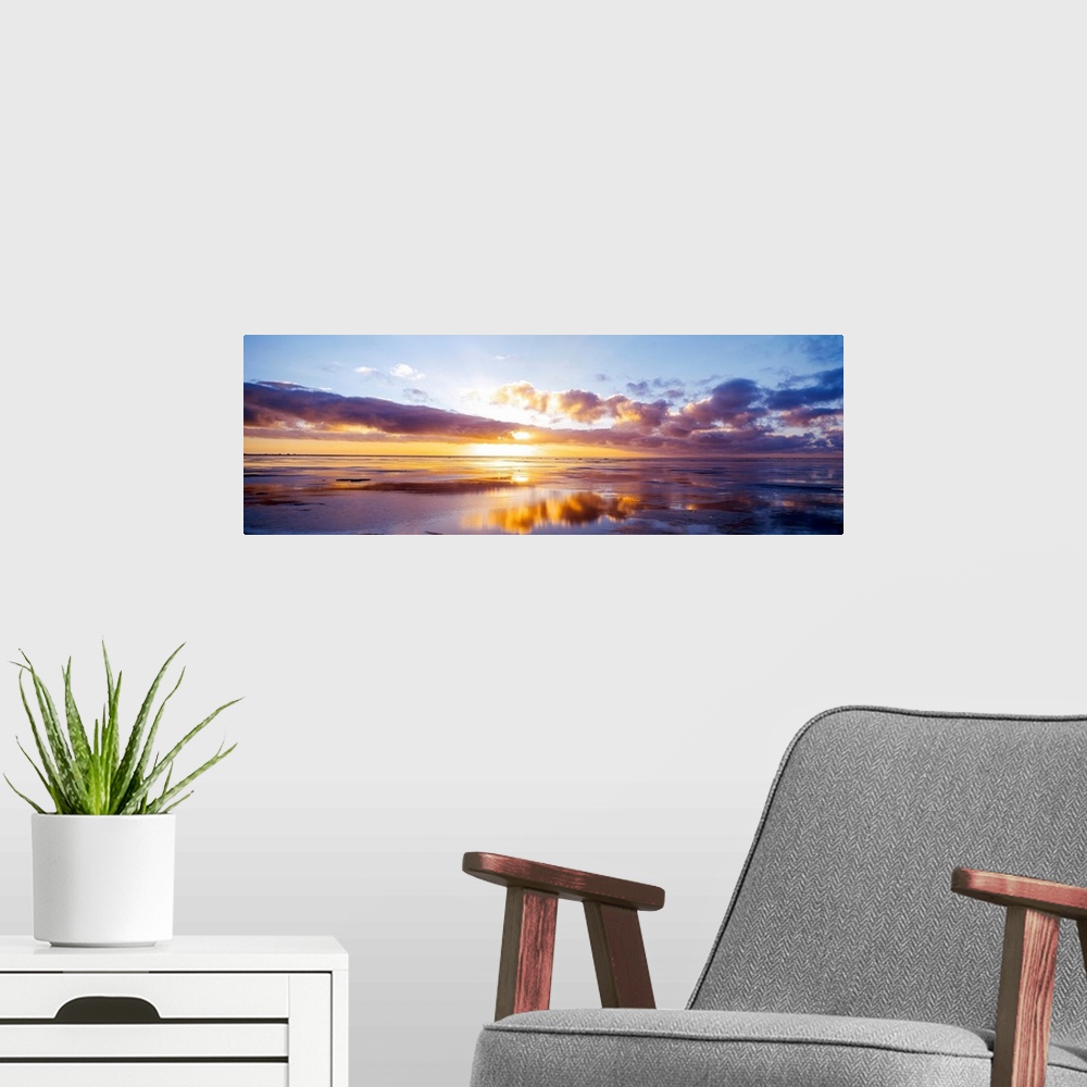 A modern room featuring The sun breaks over the clouds in the horizon in this large panoramic photo from a beach on the N...