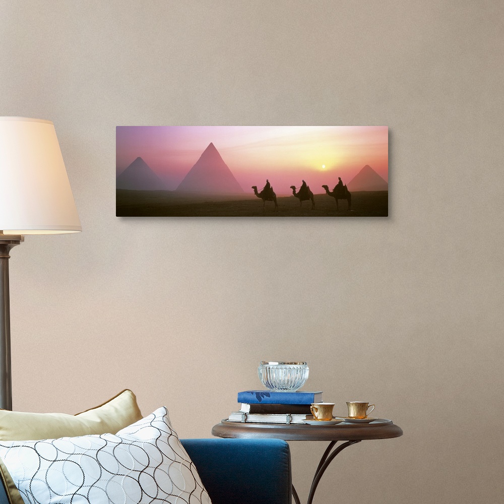 A traditional room featuring Panoramic photograph of three camel riders at dusk with pyramids in the background.  The sun is s...