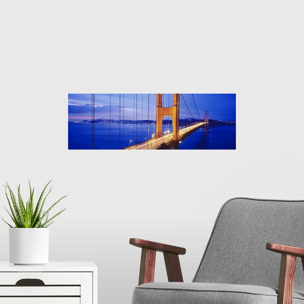 A modern room featuring Long and narrow photo print of an up close view of the Golden Gate Bridge lit up at night with ca...