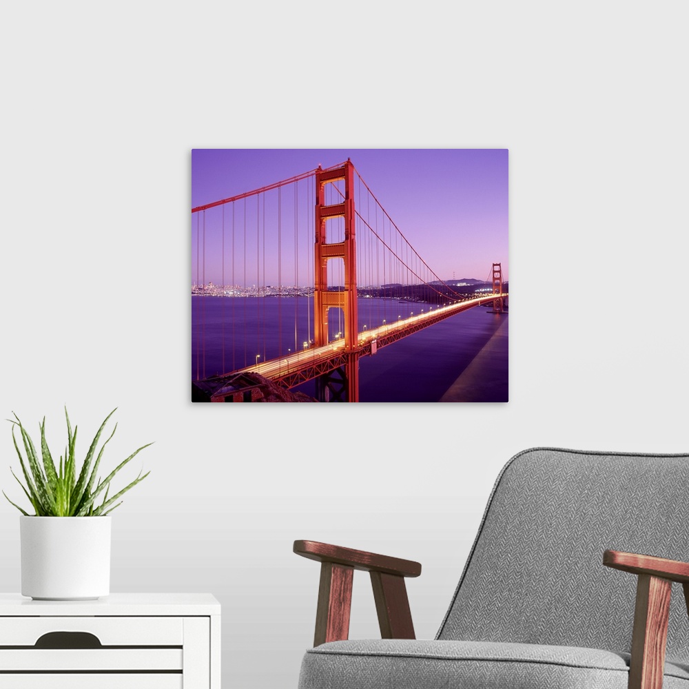A modern room featuring Cars driver over the Golden Gate Bridge in San Francisco as the setting sun creates purple hues i...