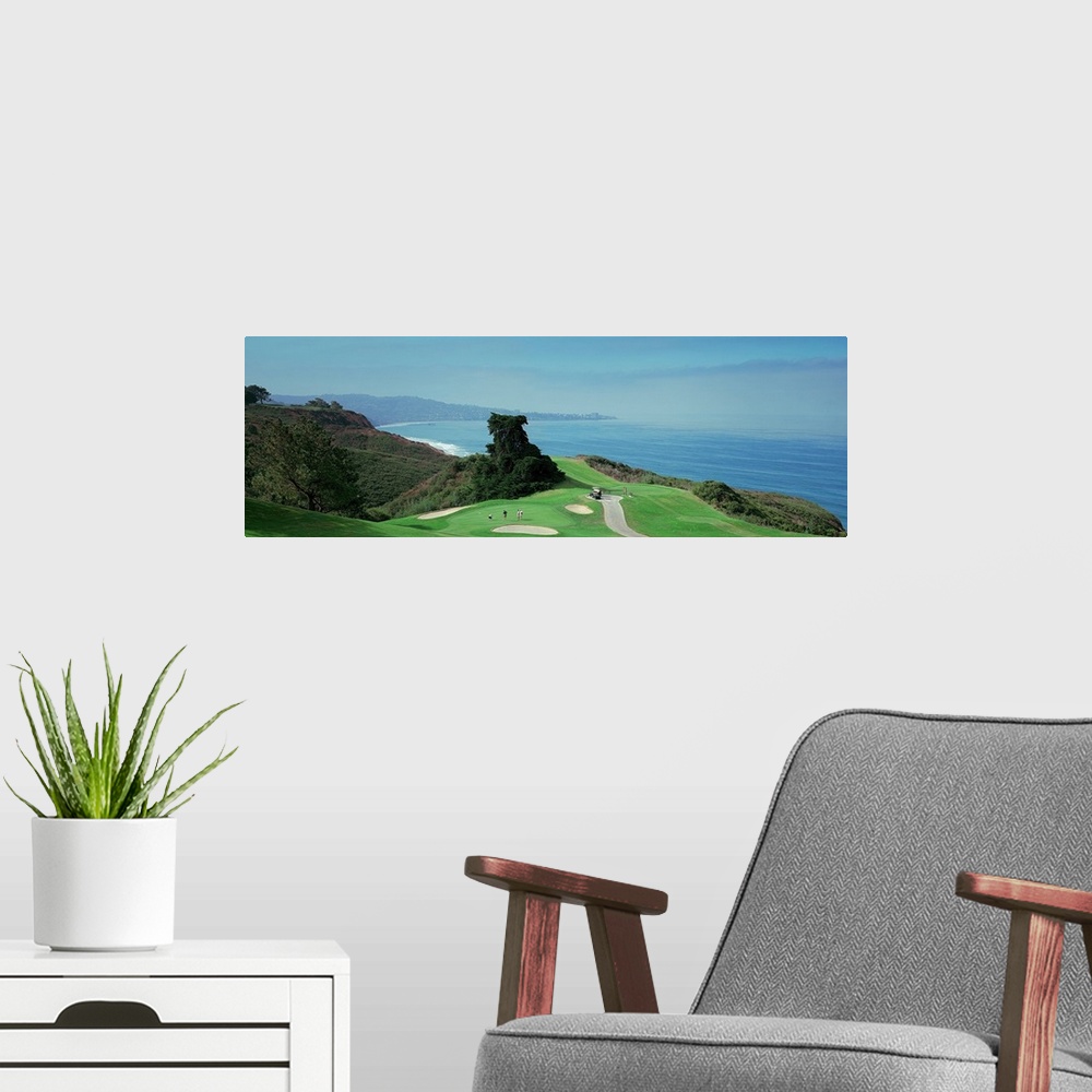A modern room featuring This wall hanging is a panoramic photograph of a golf green overlooking the ocean from the top of...