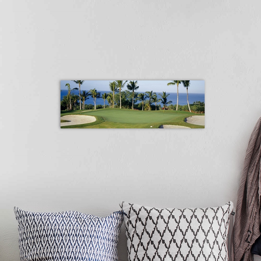 A bohemian room featuring A panormic photograph of a golf course overlooking the ocean with palm trees lining the putting g...