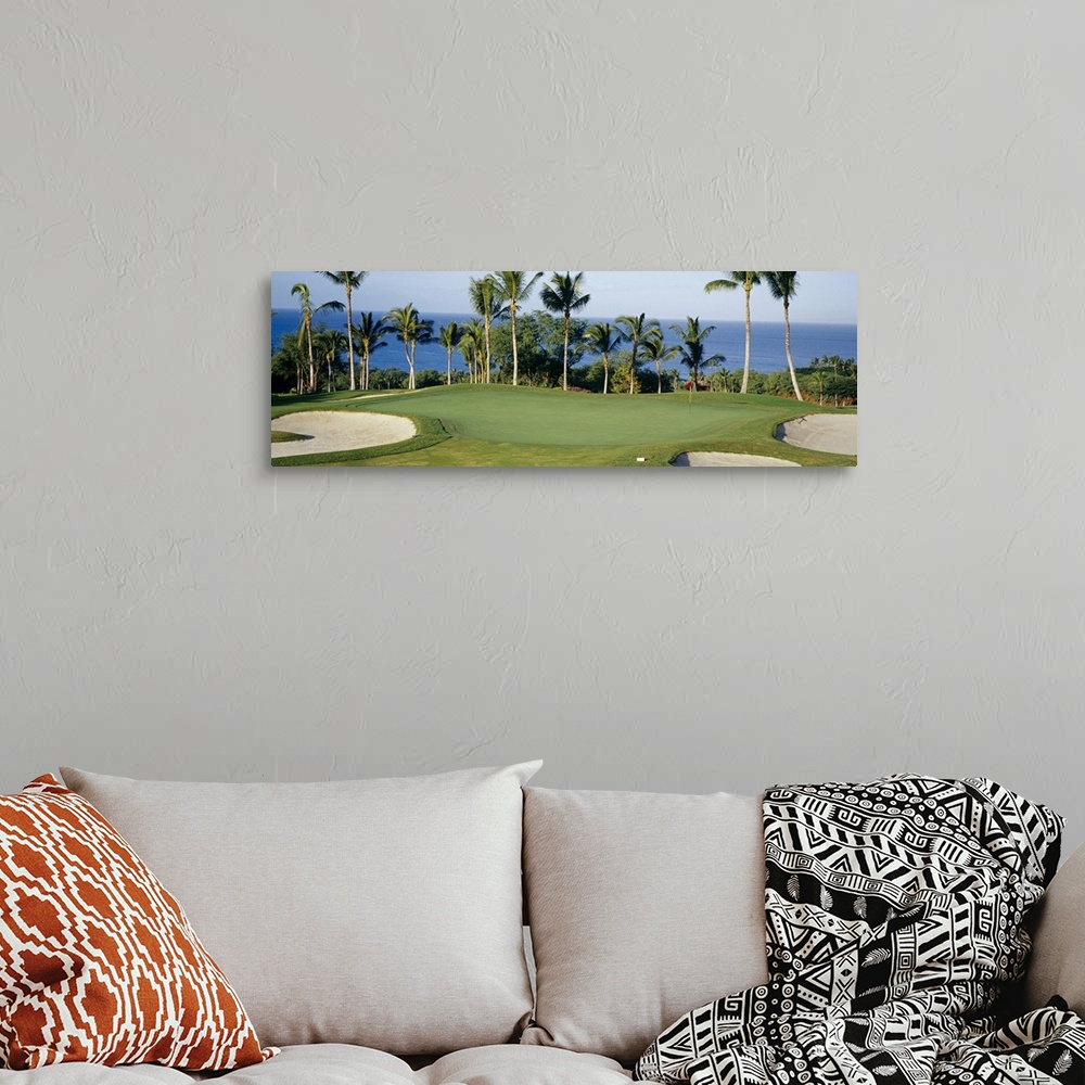 A bohemian room featuring A panormic photograph of a golf course overlooking the ocean with palm trees lining the putting g...