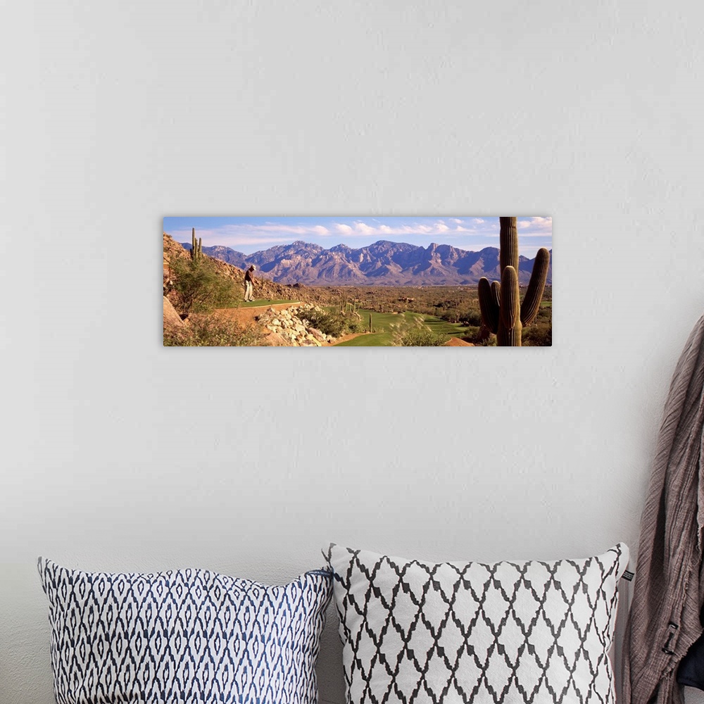 A bohemian room featuring A panoramic shot of a golfer about to tee off on a course in Arizona. Cactuses are shown on eithe...