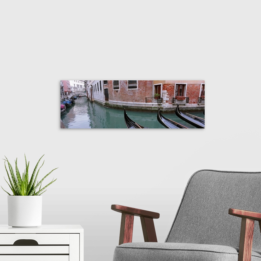 A modern room featuring The front of gondola boats are pictured in the water with buildings to either side of the canal w...