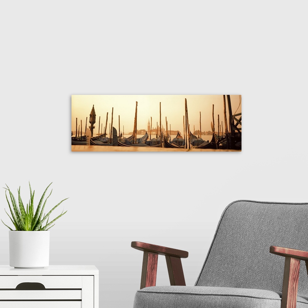 A modern room featuring A line of gondola boats are photographed in panoramic view as they sit docked in the water.