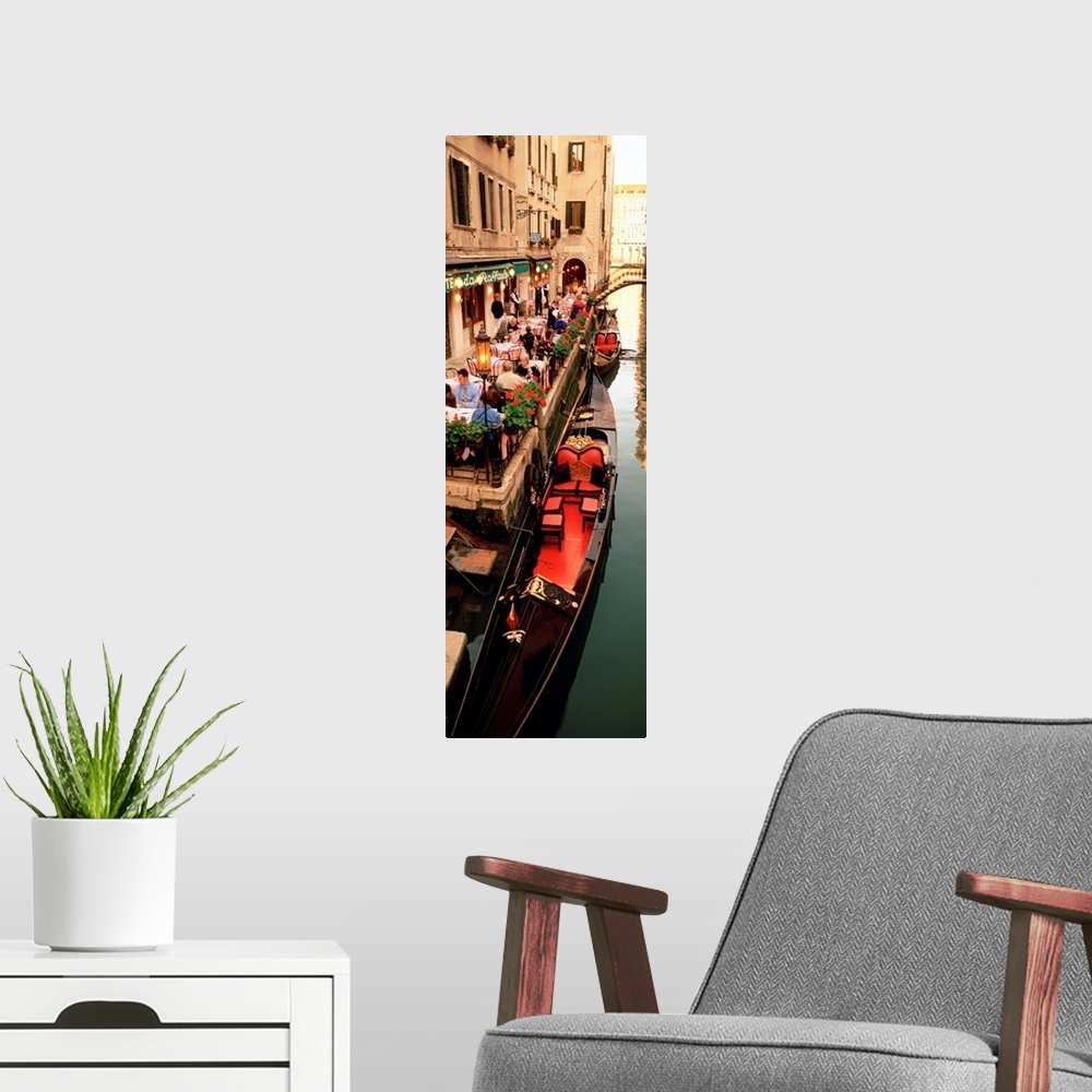 A modern room featuring Vertical panoramic photograph boats on canal waterway lined with street cafes and buildings.