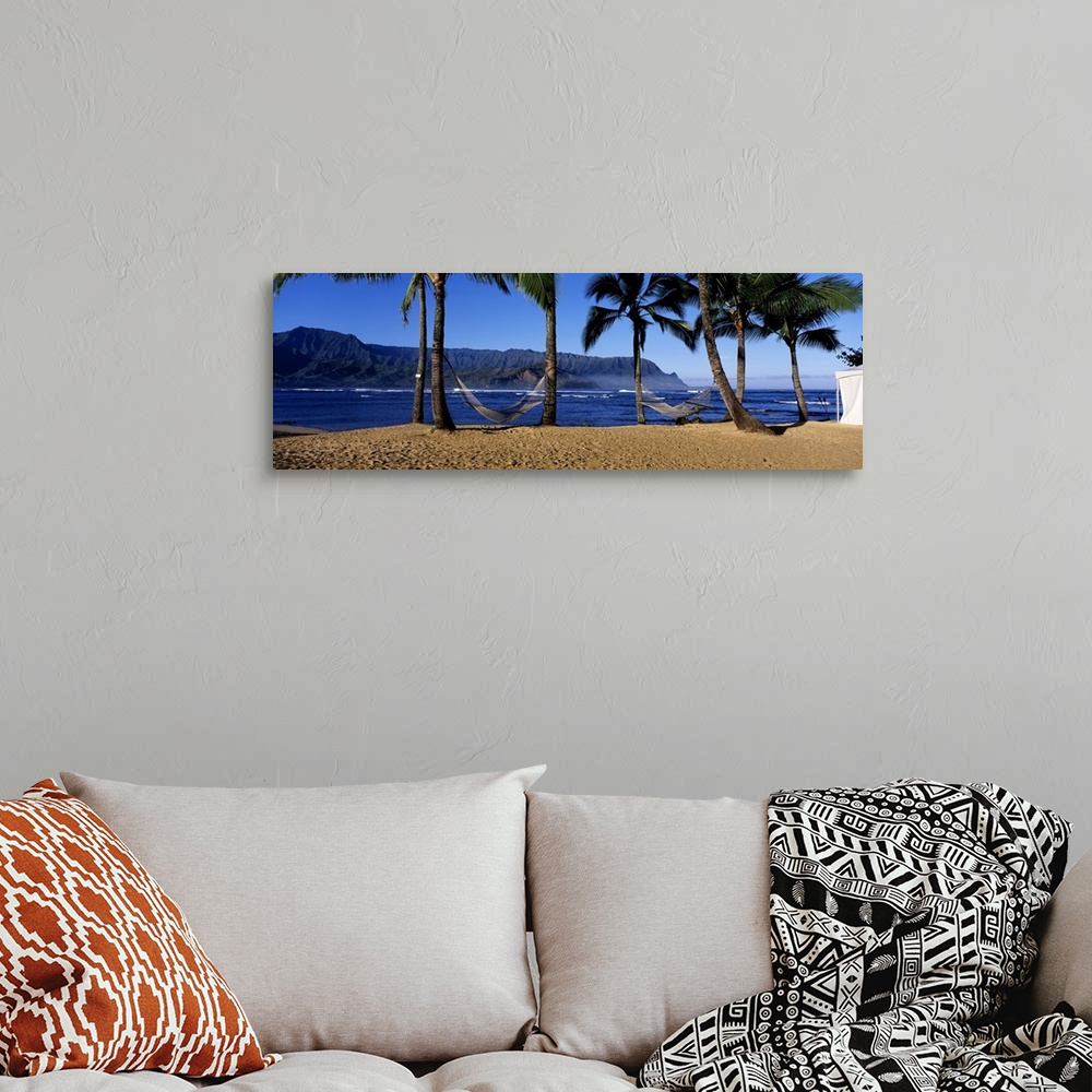 A bohemian room featuring Panoramic print of two hammocks swaying between palm trees along the ocean with mountains in the ...
