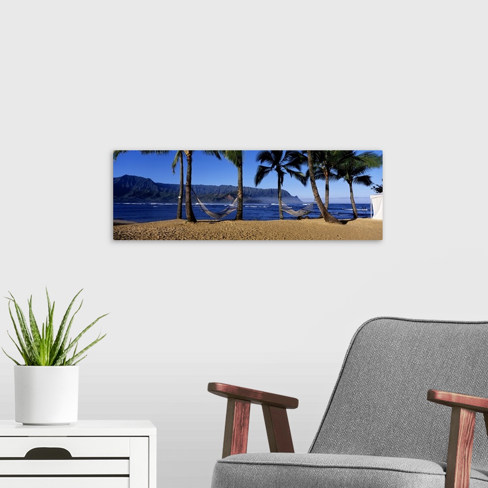 A modern room featuring Panoramic print of two hammocks swaying between palm trees along the ocean with mountains in the ...