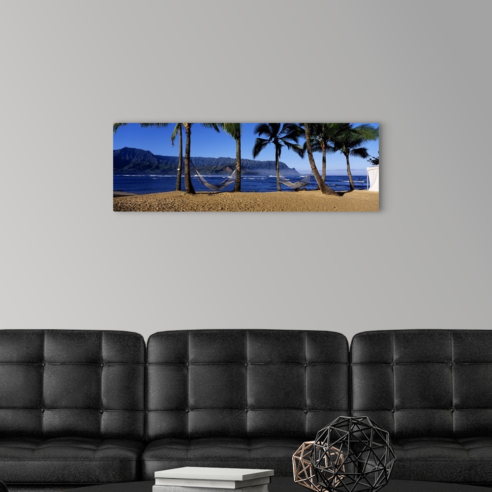 A modern room featuring Panoramic print of two hammocks swaying between palm trees along the ocean with mountains in the ...