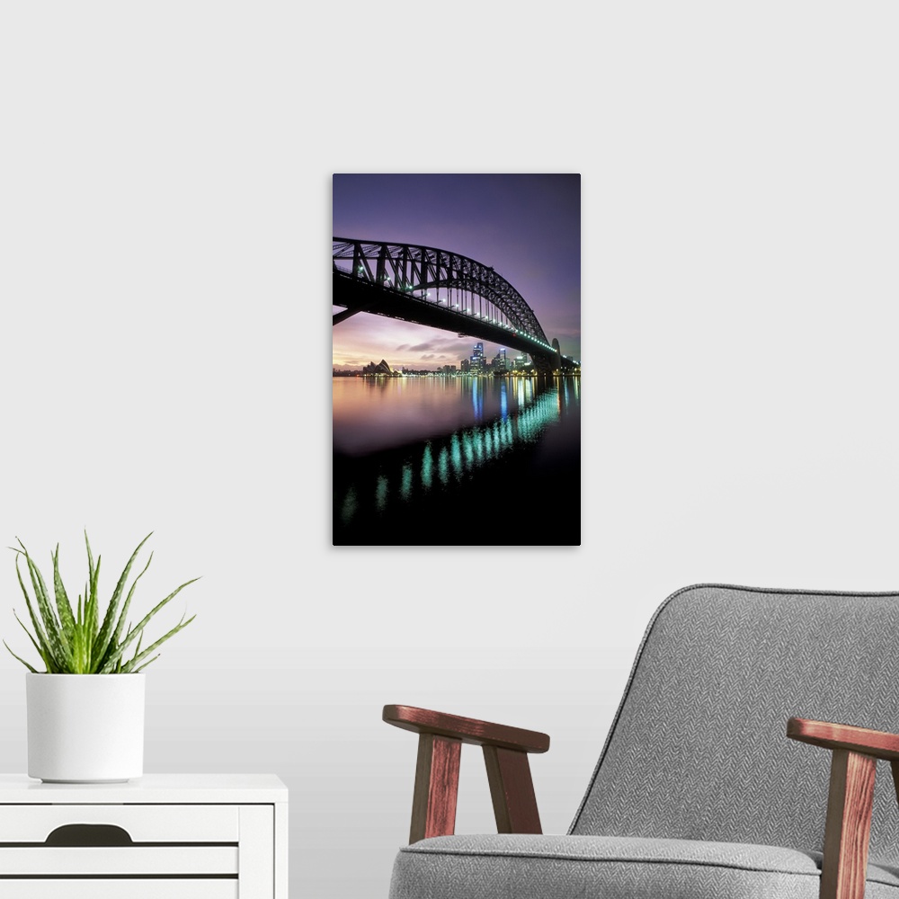 A modern room featuring Steel arch bridge crossing over the harbor in the evening, with the Sydney Opera house in the dis...