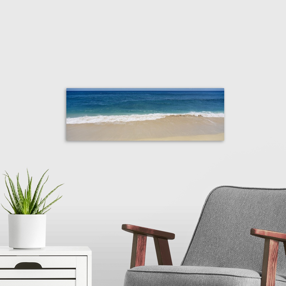A modern room featuring Long photograph of waves crashing in to the sandy beach as blue water stretches for miles in the ...