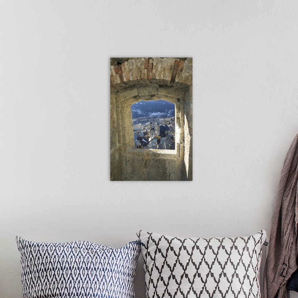 A bohemian room featuring A photograph is taken through a small stone edged window of a town below.