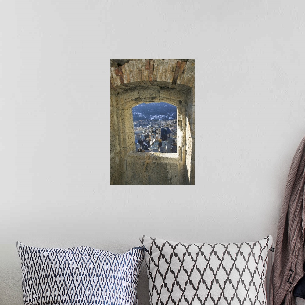 A bohemian room featuring A photograph is taken through a small stone edged window of a town below.