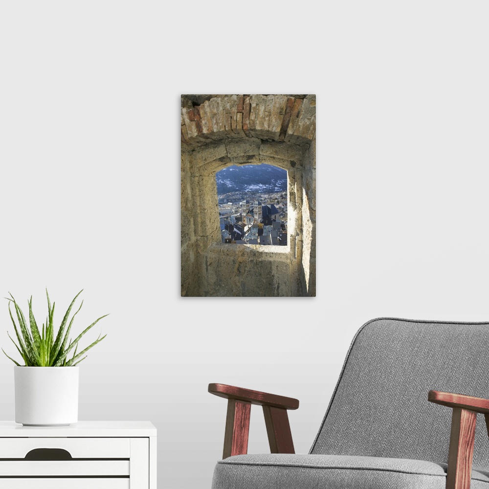 A modern room featuring A photograph is taken through a small stone edged window of a town below.