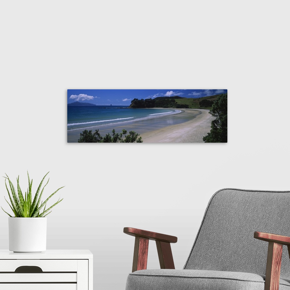 A modern room featuring This large panoramic photograph is taken from the New Zealand coast with a large hill in the dist...