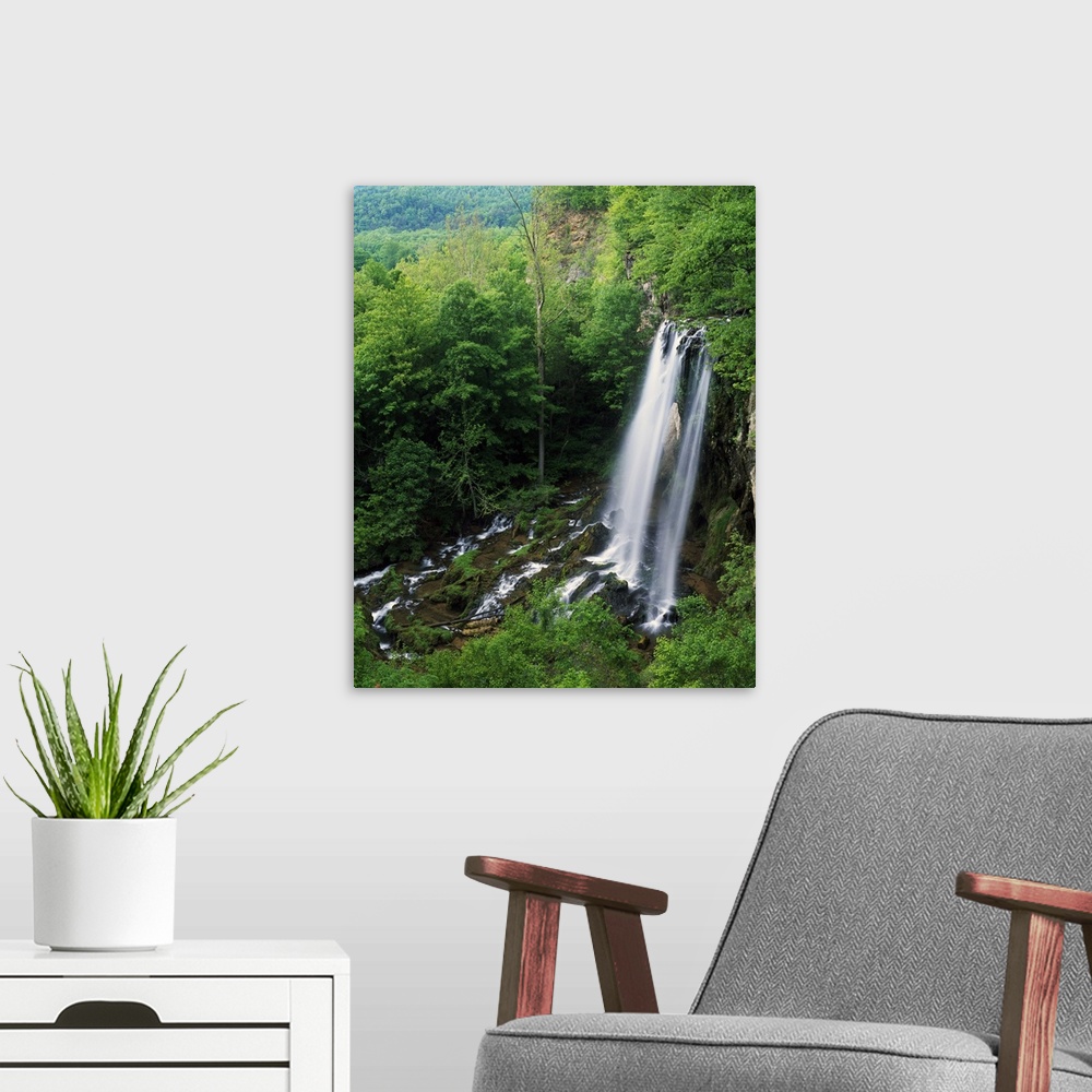 A modern room featuring A large waterfall is photographed from above as it falls onto rocks and is surrounded by thick fo...