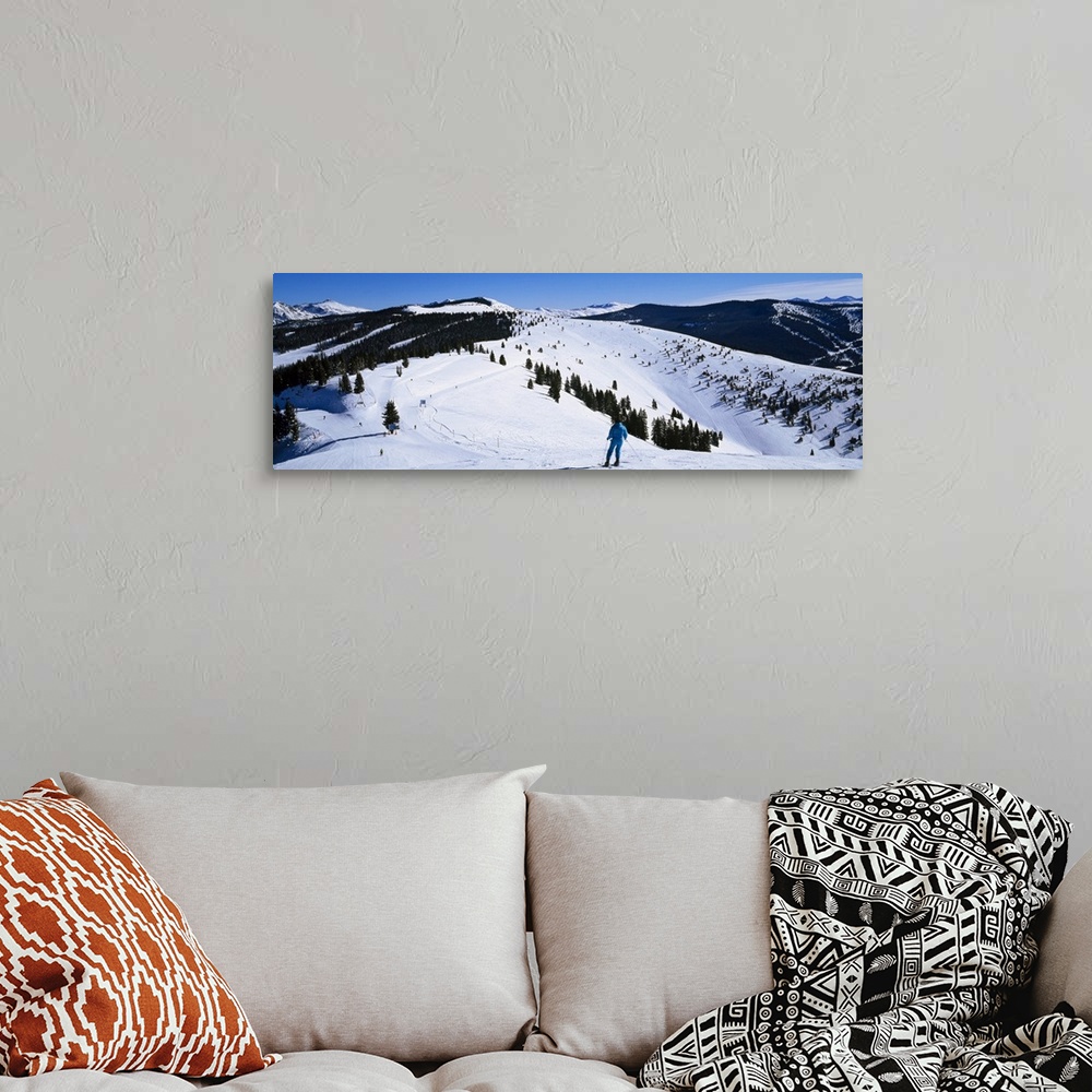 A bohemian room featuring A panoramic photograph of a skier departing down a snow covered slope at the top of a mountain.