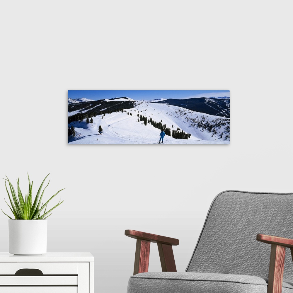 A modern room featuring A panoramic photograph of a skier departing down a snow covered slope at the top of a mountain.