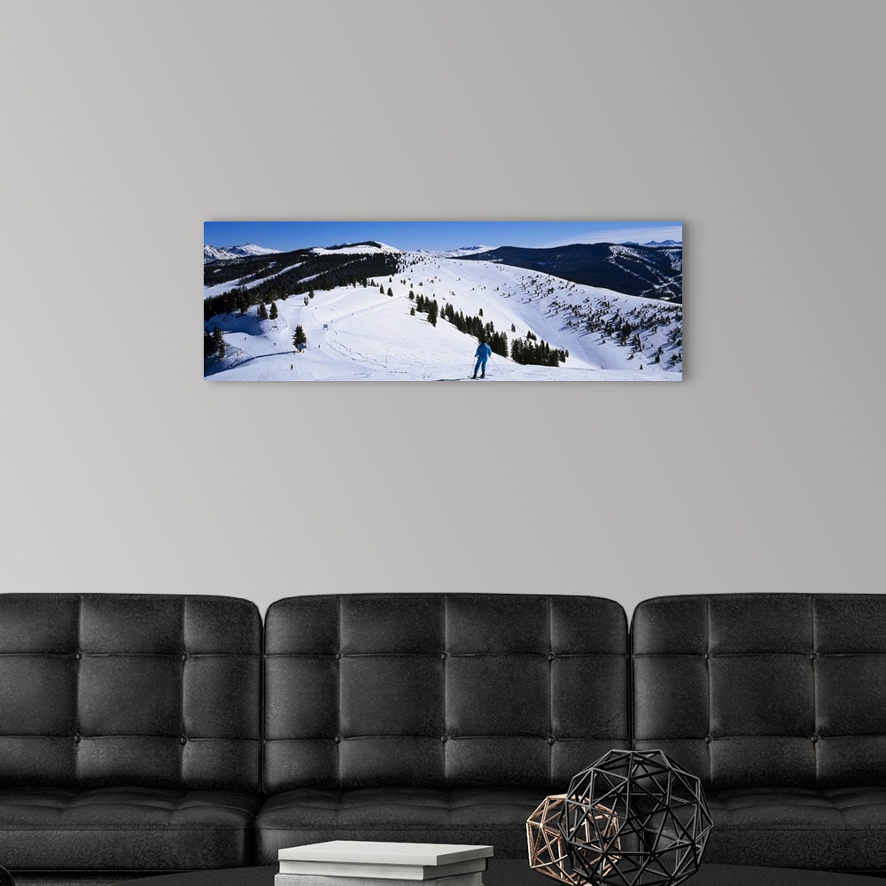 A modern room featuring A panoramic photograph of a skier departing down a snow covered slope at the top of a mountain.