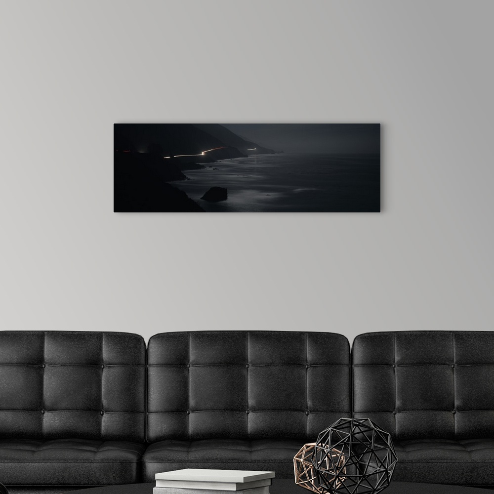 A modern room featuring Panoramic photograph of road near coastline lit up with moving headlights at night.