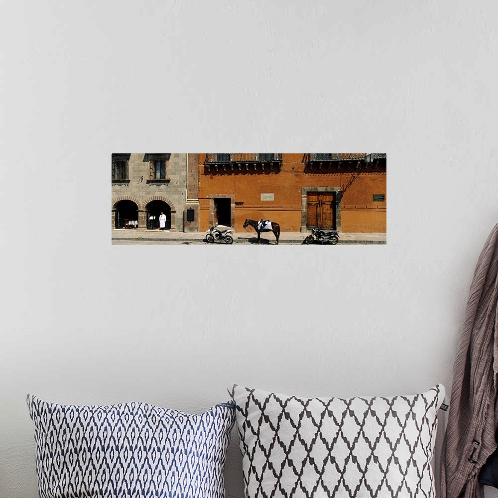 A bohemian room featuring This panoramic photograph shows two motorcycles sitting on a stone street with a horse standing i...