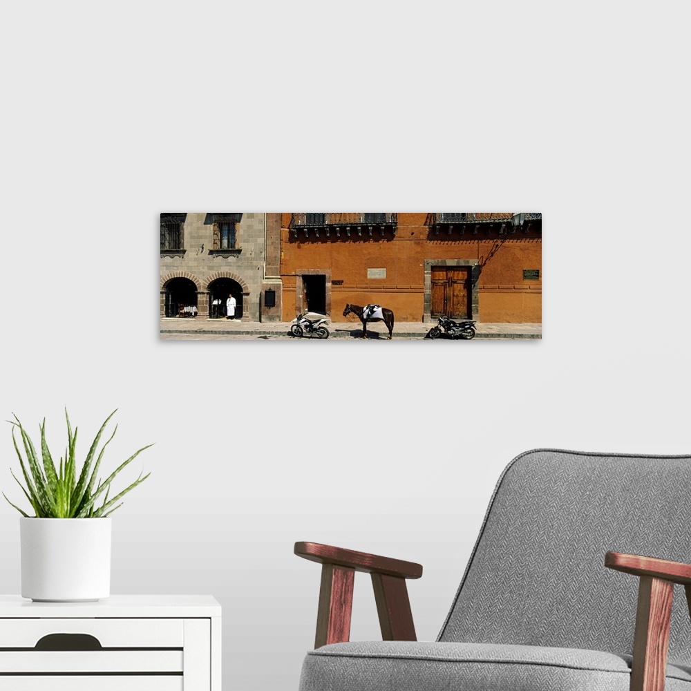 A modern room featuring This panoramic photograph shows two motorcycles sitting on a stone street with a horse standing i...