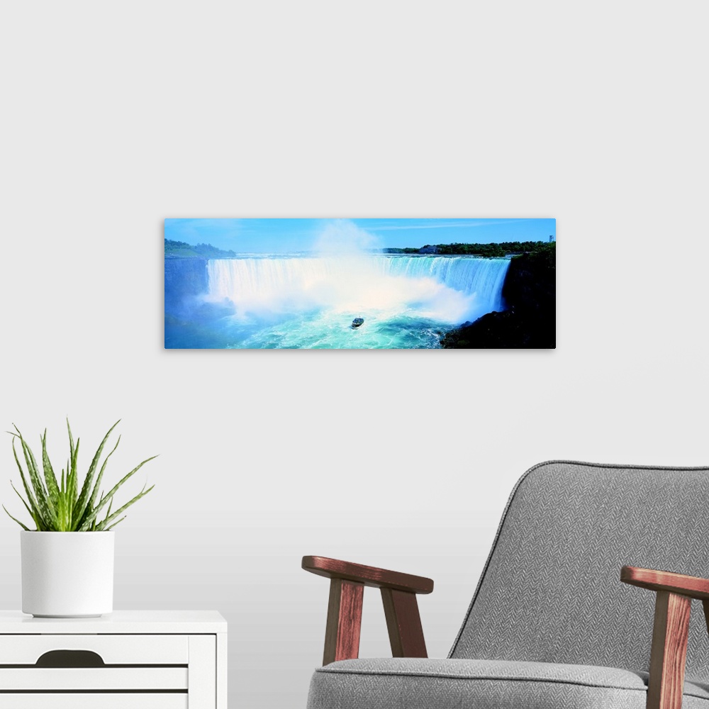 A modern room featuring Long wall art of Niagara Falls rushing downward and a boat of tourists approaching it from the bo...