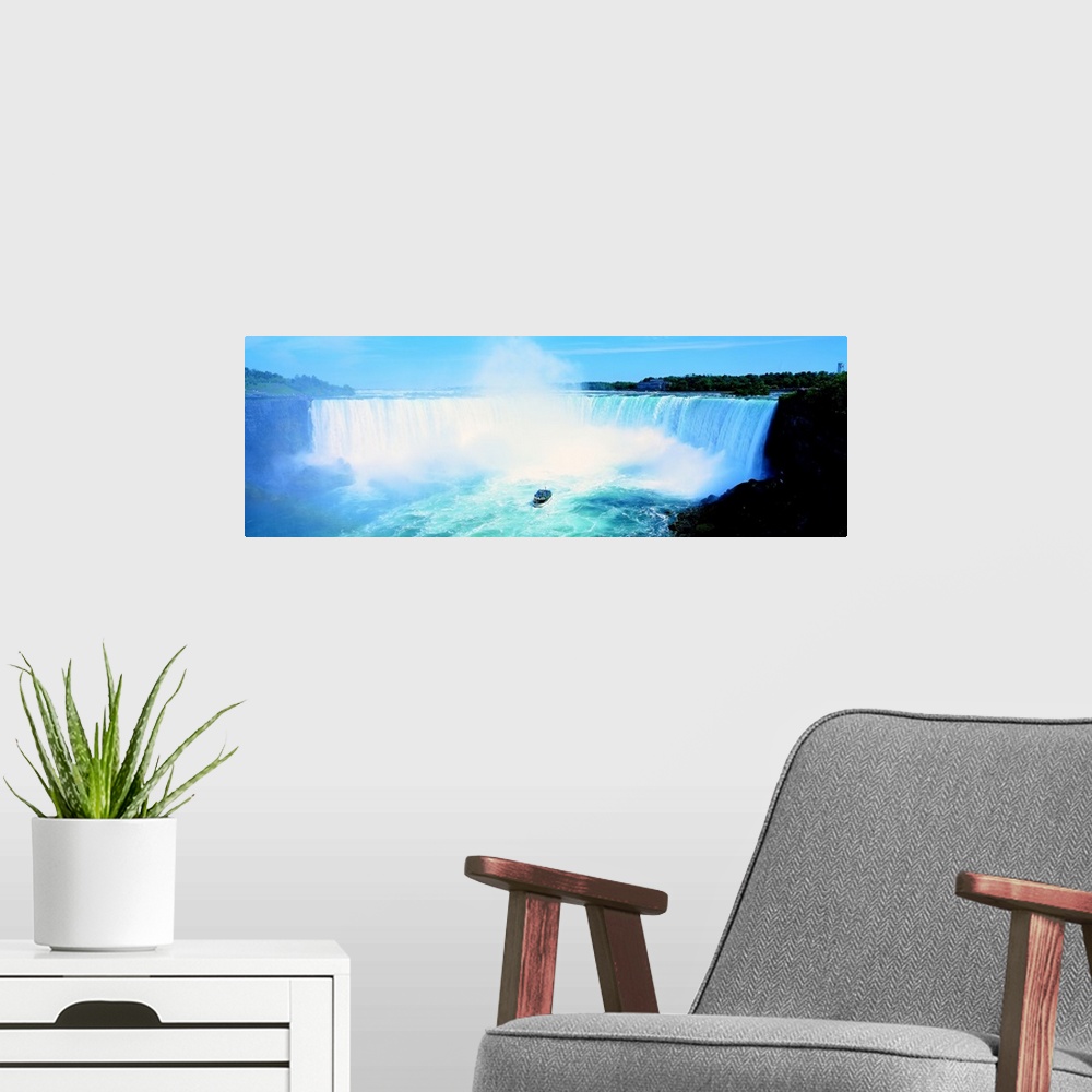 A modern room featuring Long wall art of Niagara Falls rushing downward and a boat of tourists approaching it from the bo...