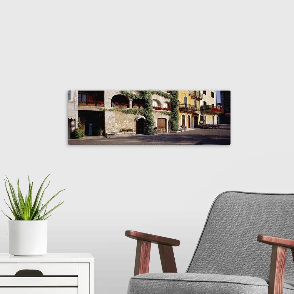 A modern room featuring Street photo of a road in Torri Del Benaco, Italy lined with ivy covered stone houses with flower...