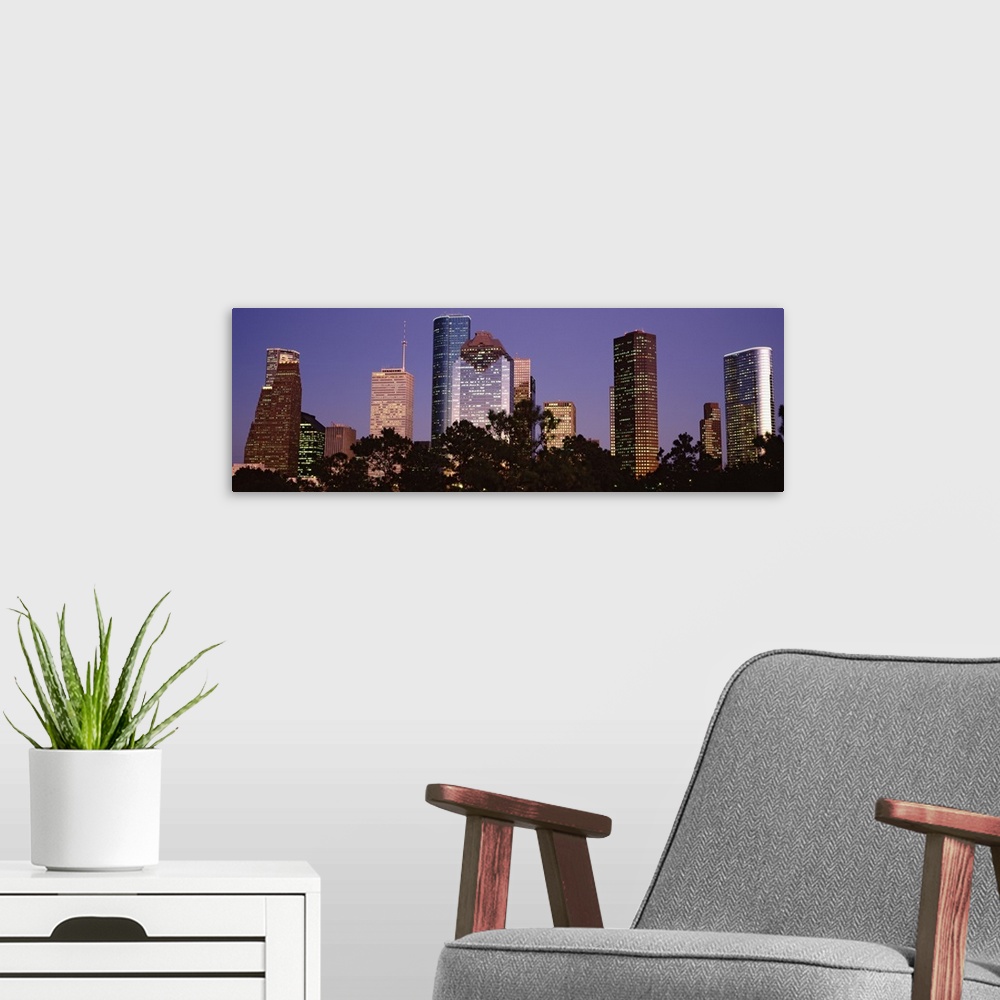 A modern room featuring A panoramic view of the Houston skyline with the buildings illuminated and trees that line the bo...
