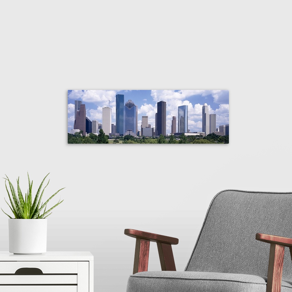 A modern room featuring Giant, landscape wall picture of the Houston skyline, under a bright blue sky with many fluffy cl...