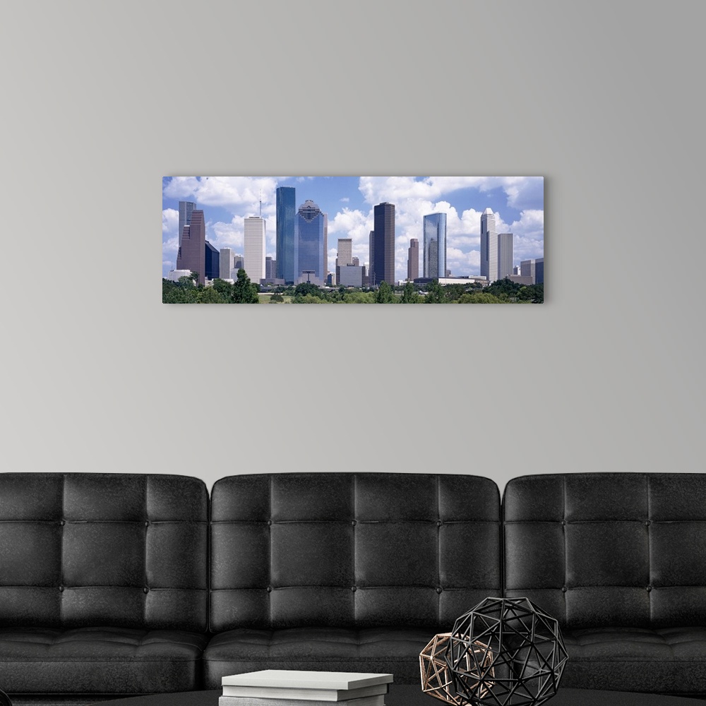 A modern room featuring Giant, landscape wall picture of the Houston skyline, under a bright blue sky with many fluffy cl...