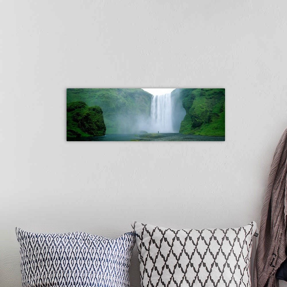 A bohemian room featuring Panoramic photo of a wide waterfall spilling over a cliff into the water below with a man standin...
