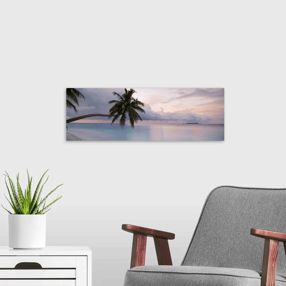 A modern room featuring Large art piece of the still ocean with a cooler toned sky above. Palm trees float over the sand ...