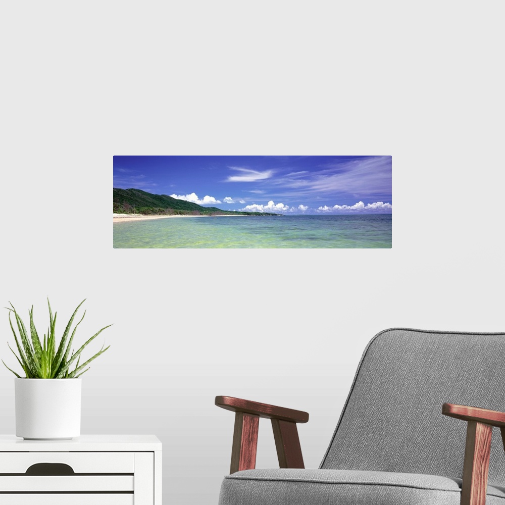 A modern room featuring Panoramic photograph of ocean with shoreline and grass covered mountains in the distance under a ...