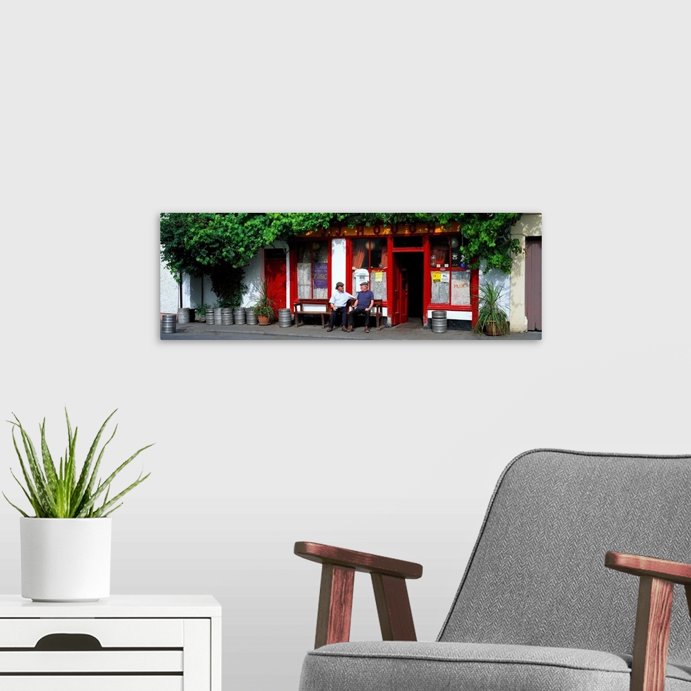 A modern room featuring Panoramic picture snapped of two men as they sit on a bench outside a bar in Ireland. The front o...