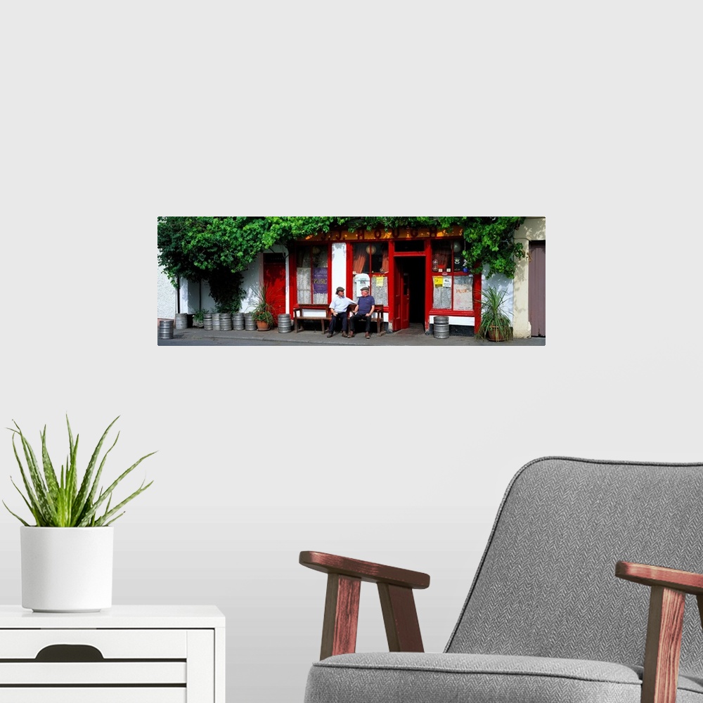 A modern room featuring Panoramic picture snapped of two men as they sit on a bench outside a bar in Ireland. The front o...