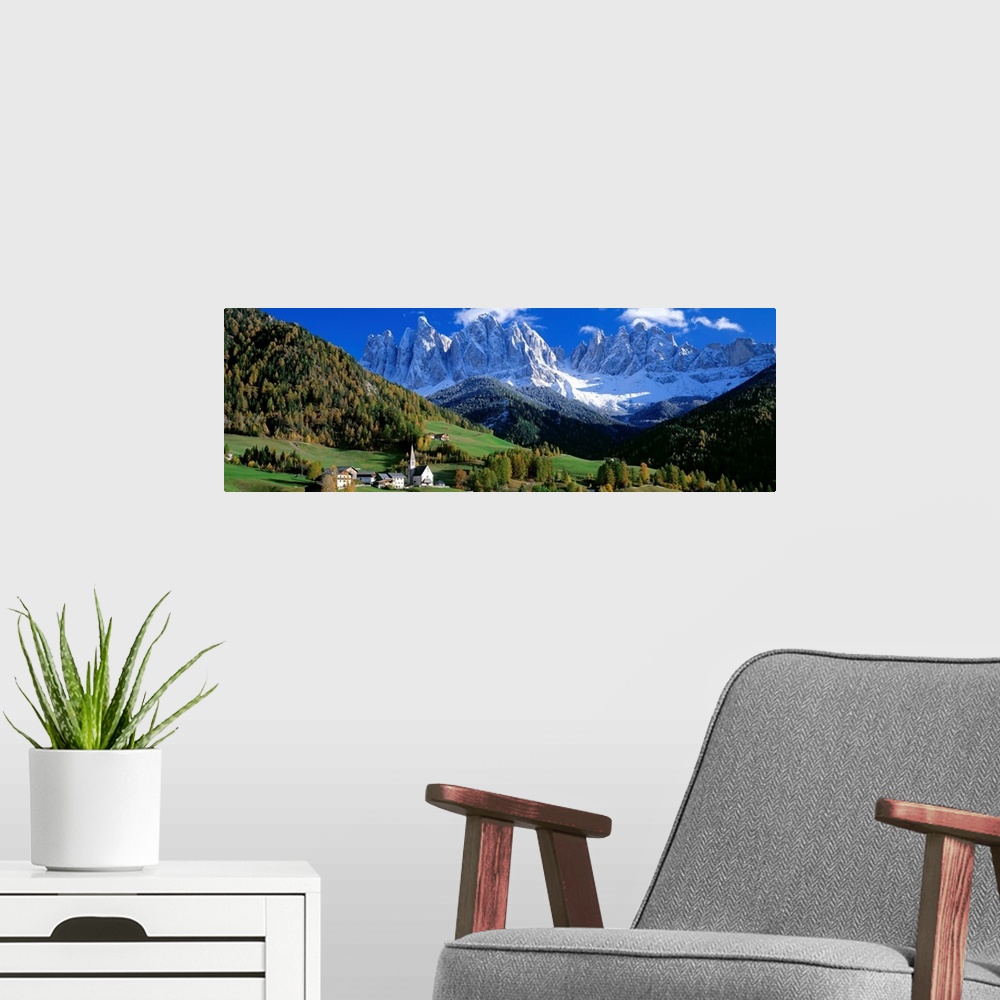 A modern room featuring The snow covered Alps tower over a quiet valley filled with conifer trees in this panoramic photo...