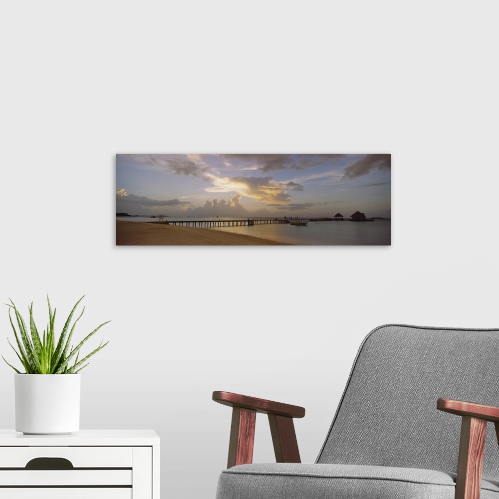 A modern room featuring Panoramic photograph of pier stretching into ocean from the beach under a cloudy sky at dusk.