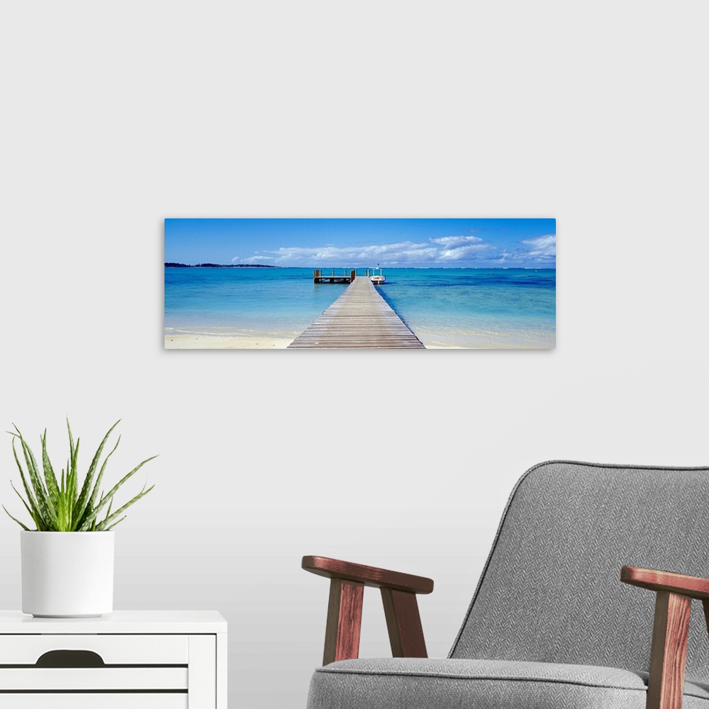 A modern room featuring Panoramic photograph of pier stretching into the sea off of a sandy beach.  There is a small wood...
