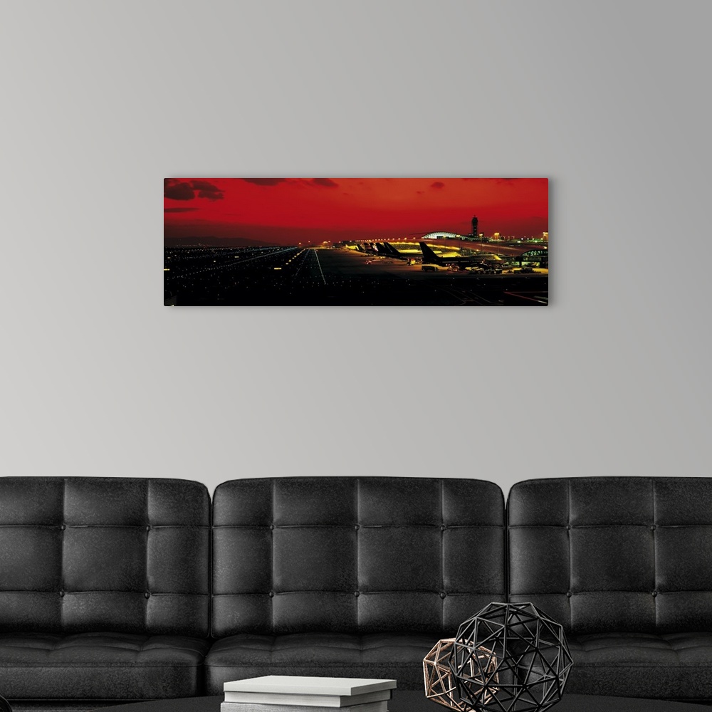 A modern room featuring High angle photograph on a horizontal wall hanging of a line of aircraft surrounded by the lights...