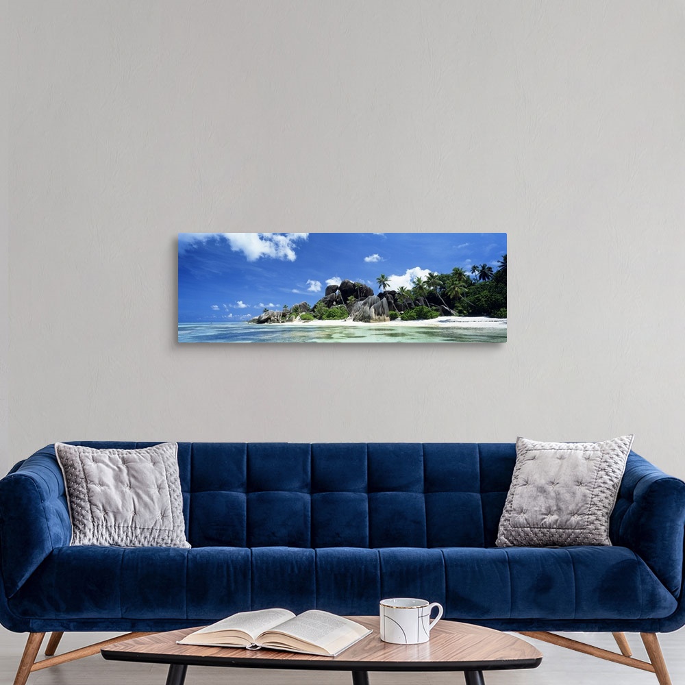 A modern room featuring A panoramic photograph of a tropical beach lined with large boulders and palm trees taken on a su...